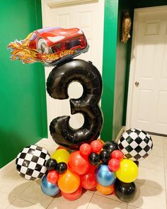 the number three is surrounded by balloons and race cars in front of a green wall