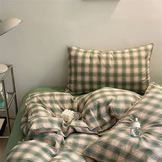 an unmade bed with green and white plaid comforter next to a night stand