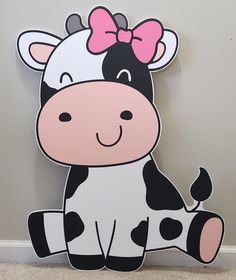 a cartoon cow with a pink bow sitting on the floor in front of a wall