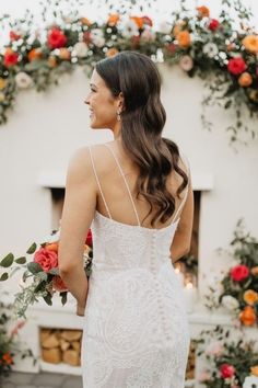 a woman standing in front of an arch with flowers on it and wearing a white dress