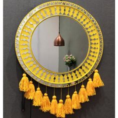 a round mirror with tassels hanging on the wall next to a flower vase