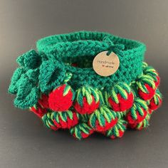 a green and red knitted basket with strawberries on the inside, sitting on a gray surface