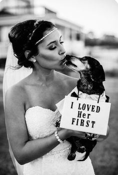 a woman in a wedding dress kissing her dog with a sign that says i loved her first