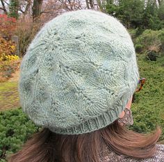 a woman with long hair wearing a green knitted hat in the park on a sunny day