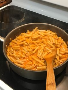 a pan filled with pasta sitting on top of a stove next to a wooden spoon