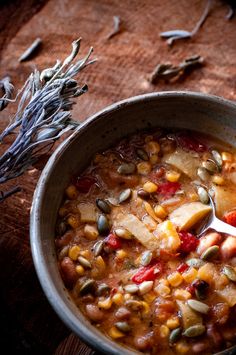 a bowl filled with beans and vegetables on top of a wooden table next to dried herbs