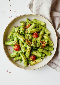 a white bowl filled with pesto pasta on top of a table next to a napkin