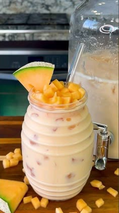 a glass filled with fruit sitting on top of a wooden table next to a pitcher