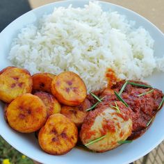 a white plate topped with rice and meat covered in sauce next to sliced banana slices