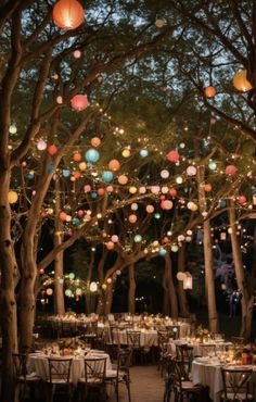 an outdoor event with paper lanterns hanging from the trees and tables set up for dinner