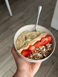 a person holding up a bowl of oatmeal and strawberries