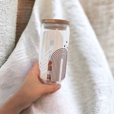 a person holding a glass with designs on it and a white blanket in the background