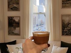 a person holding a cup of coffee in front of a window with pictures on the wall