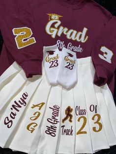 the maroon and white graduation gown is next to two matching t - shirts with gold lettering on them