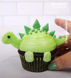 a cupcake with green frosting and a dinosaur decoration