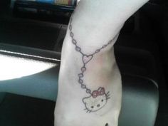 a hello kitty tattoo on the foot of a person with a cross and heart shaped beads