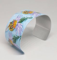 "\"The Gatherer\" image portrays a Honey Bee gathering pollen from a wildflower. This piece was created by award winning Cherokee artist, MaryBeth Timothy. The image is sublimated onto a lightweight, adjustable aluminum cuff bracelet. They are easily squeezed and pulled apart to adjust to most adult sized wrists. Dimensions: 6.5\" x 1.375\"" Hand Painted Adjustable Cuff Bracelet As Gift, Handmade Yellow Cuff Bracelet, Unique Adjustable Hand Painted Cuff Bracelet, Bumble Bee Bracelet, Multicolor Inlay Bangle Cuff Bracelet, Vintage Inlay Cuff Bracelet Bangle, Bee Bee, Bee Jewelry, Bee Art