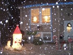 a teddy bear wearing a santa hat in front of a house on a snowy night