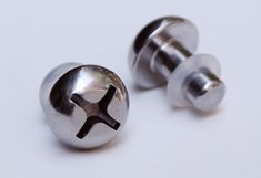 two metal screws on a white surface, one has a black star and the other is silver