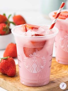 two cups filled with ice and strawberries on top of a cutting board next to some strawberries