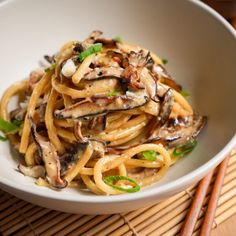 a white bowl filled with pasta and mushrooms on top of a table next to chopsticks