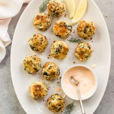 a white plate topped with crab cakes next to a bowl of dipping sauce and lemon wedges