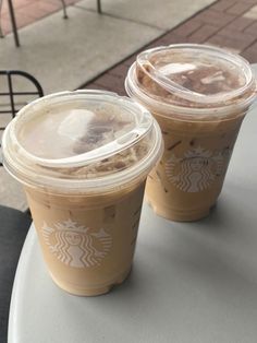 two cups of iced coffee sitting on top of a white table next to each other