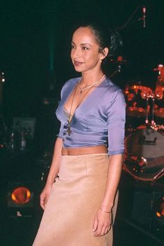 a woman standing in front of a drum set at a rock concert wearing a tan skirt