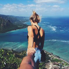 a woman standing on top of a cliff overlooking the ocean and mountains with her back to the camera