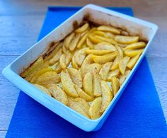 a blue dish filled with sliced apples sitting on top of a blue tablecloth next to a knife and fork