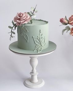 there is a green cake with pink flowers on the top and bottom, sitting on a white pedestal