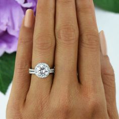 a woman's hand with a diamond ring on it and purple flowers in the background