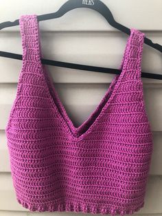 a pink crocheted top hanging on a white wall