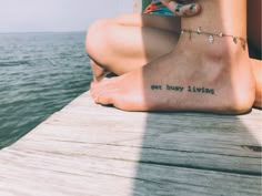 a woman's foot with the words get busy living tattooed on it sitting on a dock