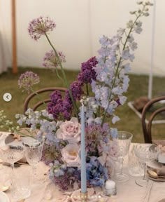 an arrangement of flowers in a vase on a table with glasses and plates around it