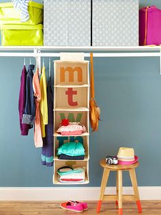 an organized closet with clothes hanging on the rack and shoes sitting on the stool next to it