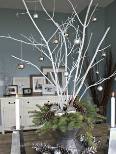 a christmas tree with white branches and ornaments in a silver bowl on a table next to a dresser