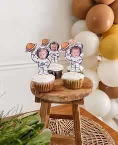 two cupcakes sitting on top of a wooden table next to a balloon wall