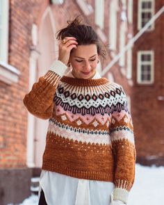 a woman walking in the snow with her hand on her head and wearing a sweater