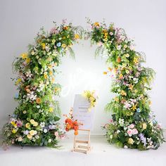 an arch made out of flowers and greenery with a sign in the foreground