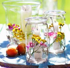 three glass vases filled with flowers and candles