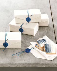 four white boxes tied with blue twine on top of each other next to some cookies