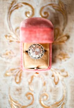 an engagement ring in a pink velvet box on a gold and white damask background