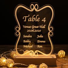 a glass table number holder with lights around it on a wooden surface, surrounded by string lights