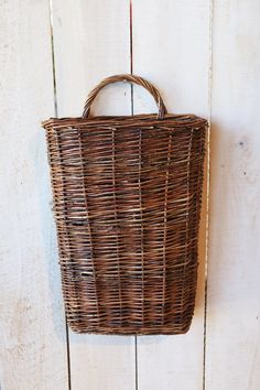 a wicker basket hanging on the side of a white wooden wall with an iron hook