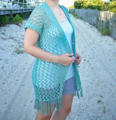 a woman is standing on the beach wearing a crocheted shawl