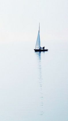 a lone sailboat floating in the middle of the ocean on a foggy day