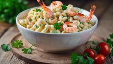 a bowl filled with pasta and shrimp on top of a cutting board next to tomatoes