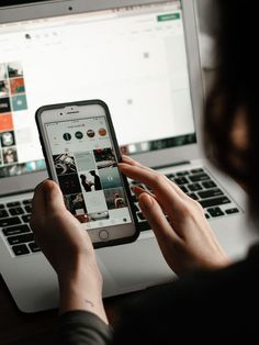 a person is looking at their cell phone while sitting in front of a laptop computer