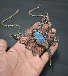 a person is holding a necklace with a bird on it's back and an intricate design